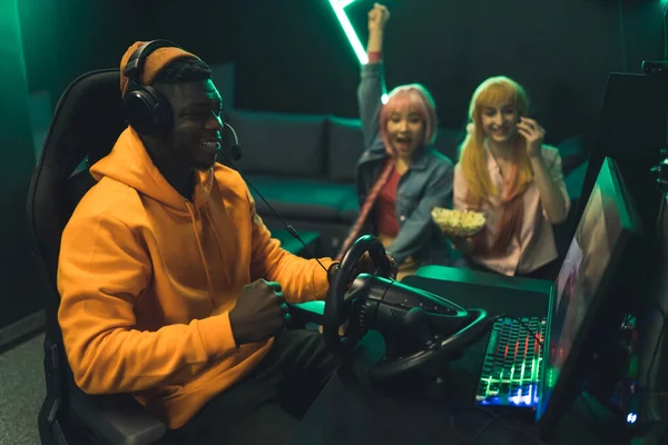 Teenagers celebrating winning a racing game. Black teenage boy wearing orange hoodie and headset sitting in gaming chair. Professional setup with steering wheel. High quality photo