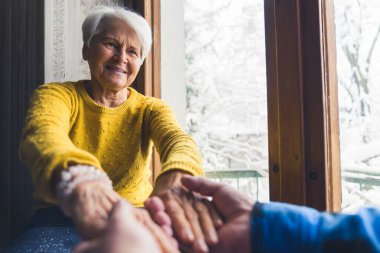 Sweet caucasian European senior couple holding hands while sitting near the window during winter . High quality photo