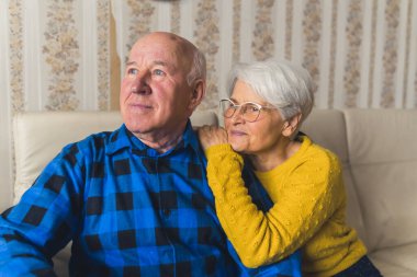 Portrait of an elderly couple - caring husband standing behind his happy loving wife and hugging her, and a woman herself softly touching his arm. High-quality photo