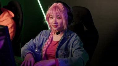 Teenage asian pink-haired girl wearing headset using professional gaming setup focused on playing online team game. . High quality 4k footage