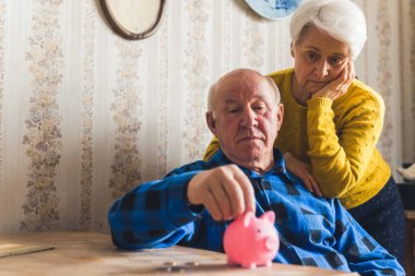 Sad, lost and worried caucasian senior couple counting coins taken out from a piggy bank while sitting by the table. Financial Crisis. High quality photo