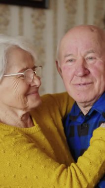 Loving old senior family couple in love smiling and hugging in the living room at home, enjoying their retirement. Vertical. High quality 4k footage