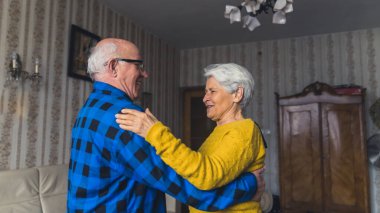 Joyful active old couple dancing and laughing in the living room, having fun at home. High quality photo