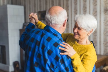 Cute caucasian elderly married couple dancing together in the middle of their house. High quality photo