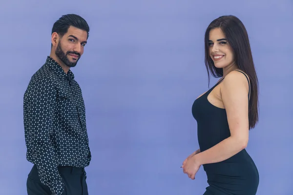 Hispanic man wearing patterned shirt looking seductively into camera standing in front of woman with long hair wearing black dress smiling. Studio shot. High quality photo