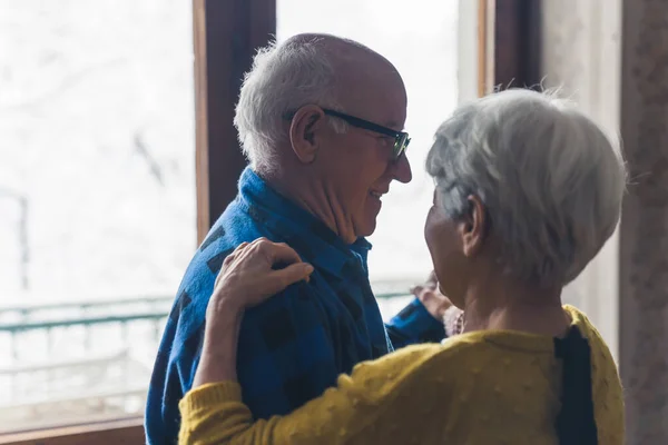 Sweet senior European married couple laughing and dancing in the living room, holding hands, spending time together during cold winter days. High quality photo