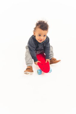 cute excited african american toddler boy sitting on the skateboard - white background. High quality photo