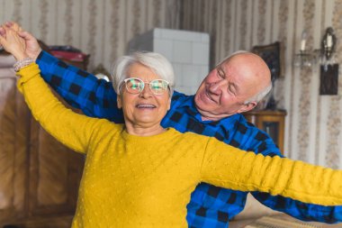 Cute joyful senior European married couple dancing, laughing, and having fun in the living room, holding hands, enjoying retirement together. High quality photo