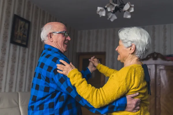 Happy romantic old married couple laughing and dancing in the living room, holding hands, having fun in retirement. High quality photo
