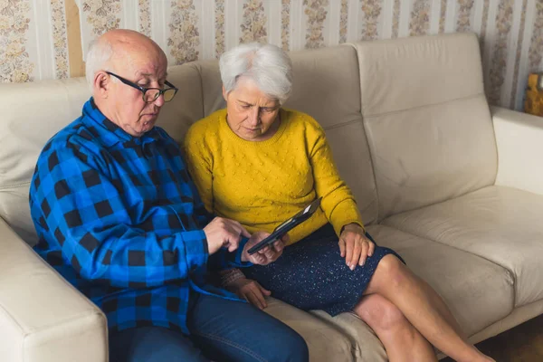 Caucasian senior confused couple trying to learn how to use a smartphone while sitting on a sofa in the living room. High quality photo