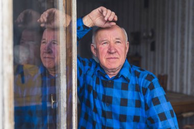 Old caucasian retired gray-haired man staring out the open window. High quality photo