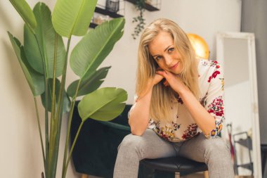 Caucasian blonde woman with long hair resting head on hands. Warm inviting look into camera. Listening closely. Indoor shot. High quality photo