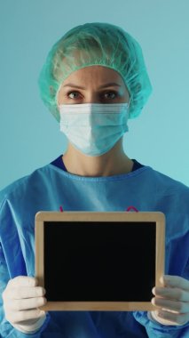 Vertical shot of a female surgeon dressed in protective medical suit holding the chalkboard with copy space. High quality 4k footage