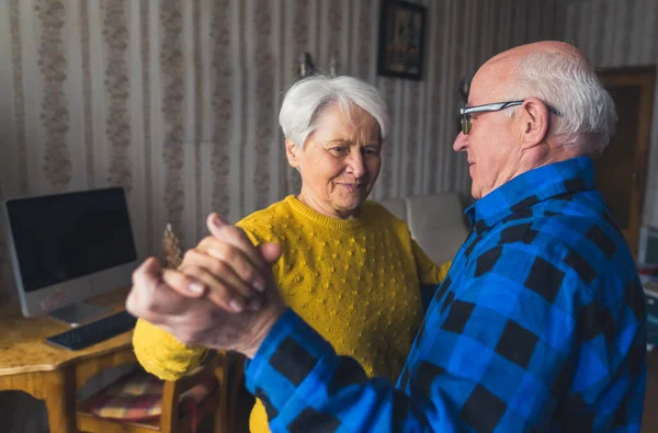 Happy caucasian elderly woman dancing with her husband together in the living room of their own house. High quality photo