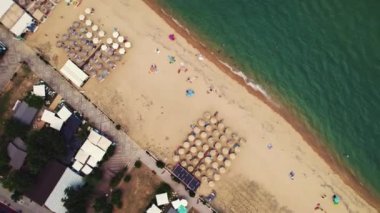 The famous Sarti resort town in South Sithonia, Halkidiki, Greece. Coastline resort, wavy Mediterranean sea crushing on the long sandy beach, people relaxing by sunbeds and umbrellas. Aerial drone
