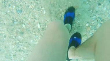 Underwater shot of a man and his feet in aquashoes walking in crystal clear sea water on a rocky sandy bottom surface. High quality 4k footage