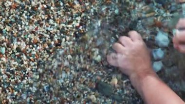 A toddler hands playing with stones and seashells barefoot on a rocky beach in the crystal clear wavy sea water in Greece. High quality 4k footage
