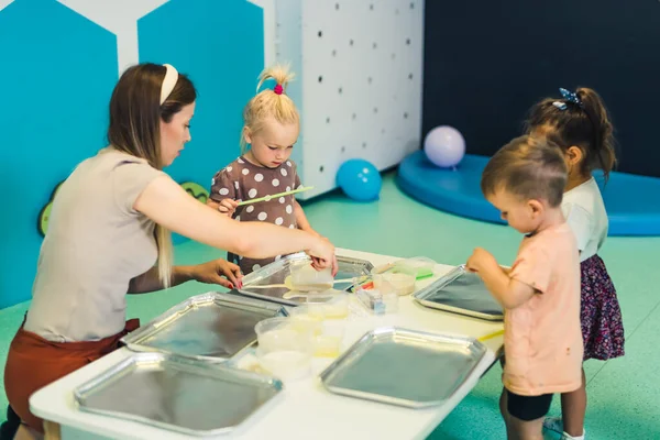 Sensory play at multi-cultural nursery school. Toddlers with their teacher playing with striped straws and milk painting, using food coloring, milk, watercolor paper, and trays. Creative kids activity