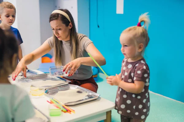 Multi-cultural nursery school. Toddlers with their teacher playing with striped straws and milk painting, using nontoxic food coloring for colors, milk, watercolor paper, and trays. Creative kids