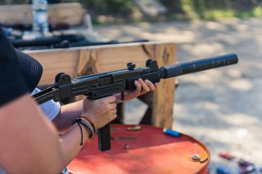 Unrecognizable young person holding uzi gun training on shooting range under supervision. Horizontal outdoor shot. High quality photo