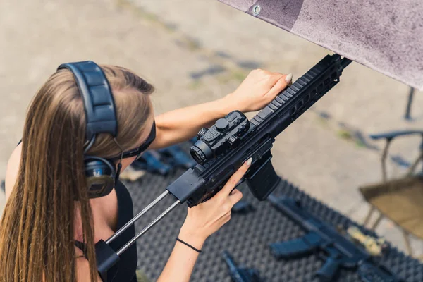 Brunette white woman in safety headphones pracrticing using submachine gun on outdoor firing range, Horizontal shot. . High quality photo