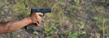 Side view of arms stretched out aiming handgun. Gun training at outdoor shooting range. Wide horizontal shot. High quality photo