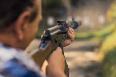 2022.08.07 Modlin, Poland - Rear view of man training aim on shooting range using ak47. Blurred foreground. Outdoor horizontal shot. High quality photo