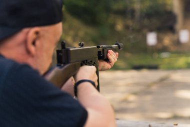 2022.08.07 Modlin, Poland - Unrecognisable man wearing black clothes training with thompson submachine gun on outdoor shooting range. Blurred background. Horizontal shot. High quality photo