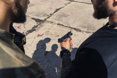 Rear view of man in black t-shirt instructing client wearing camo t-shirt how to use handgun. Firearms training. Horizontal outdoor shot. High quality photo