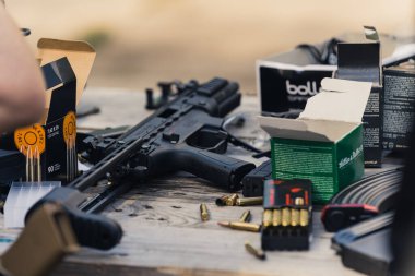 2022.08.07 Modlin, Poland - Submachine gun and various bullets and clips stored in cardboard boxes on wooden table. Military equipment and weaponry. Horizontal shot. High quality photo