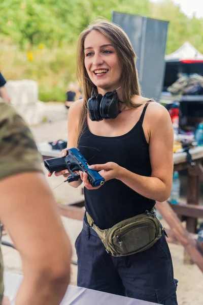Smiling white woman with safety headphones around neck buying handgun from man. Buying and selling firearms topic. Outdoor vertical shot. High quality photo