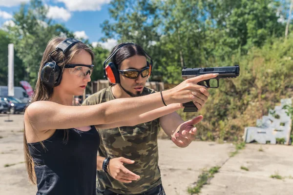 Bearded white man instructing woman how to use and aim hangun. Safety gear. Firearms training. Target practice. Horizontal outdoor shot. High quality photo