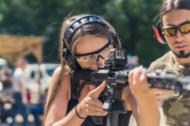 Male instructor observing woman in safety gear using submachine gun. Target practise. Firearms training at outdoor shooting range. Horizontal shot. High quality photo