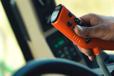 Closeup shot of red remote control with black buttons used by caucasian hand covered with dirt. Combine harvester operator. Blurred background. High quality photo