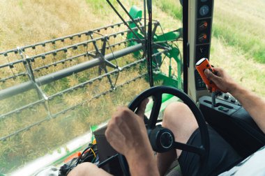 Unrecognizable caucasian male combine harvester operator driving the agricultural machine with one hand and using a special remote control with the other. High quality photo