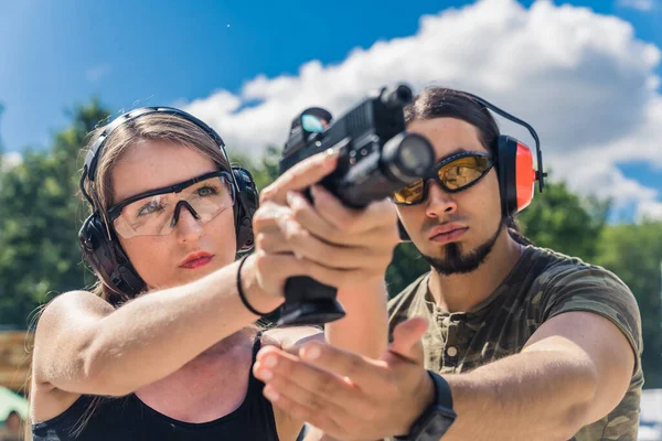 White bearded man in camo t-shirt instructing caucasian woman how to aim handgun. Safety gear. Firearms training. Target practice. Horizontal shot . High quality photo