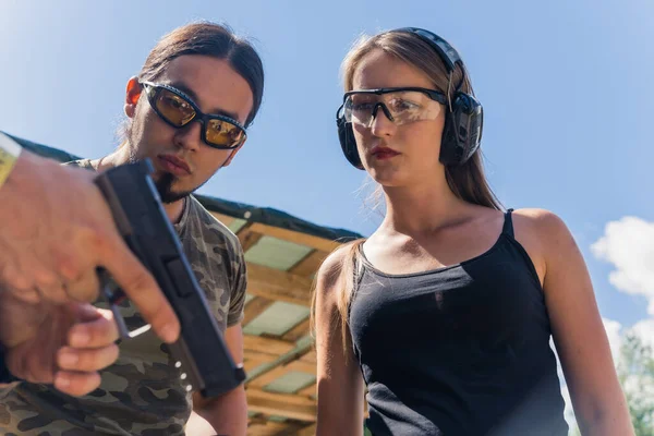 Caucasian man and woman wearing safety goggles listening to instructor showing how to operate handgun. Firearms training. Horizontal shot. High quality photo