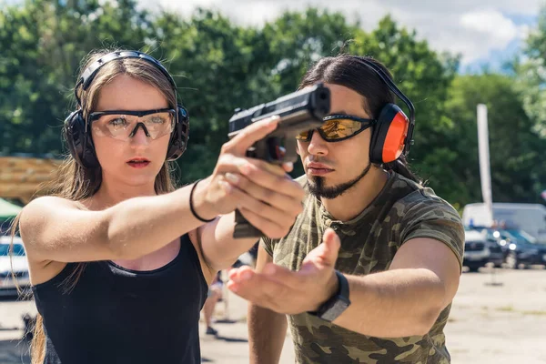 White bearded man instructing caucasian woman how to aim handgun. Safety gear. Firearm training at firing range. Outdoor horizontal shot. High quality photo