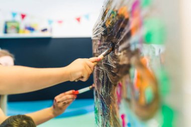 Close up toddlers hands. Cling film painting. Children painting with brushes and paints on a cling film wrapped around the wooden shelving stand. Fun useful activity for kids sensory skills