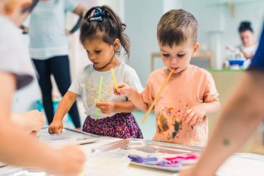 Multi-ethnic group of toddlers milk painting with the teacher helping them, using food coloring for colors. Children finger painting at the nursery school class. High quality photo