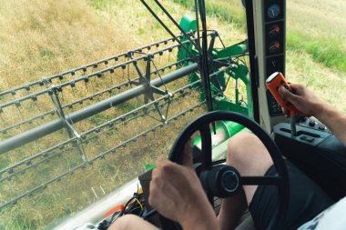 View from the combine drivers cabin - a combine header harvesting oilseed rape during late summer or autumn. A farmers hands on the steering wheel. High-quality photo