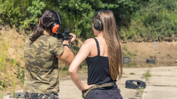 White woman and man wearing safety gear at outdoor shooting range practicing firing submachine gun. Firearms training. Horizontal shot. High quality photo