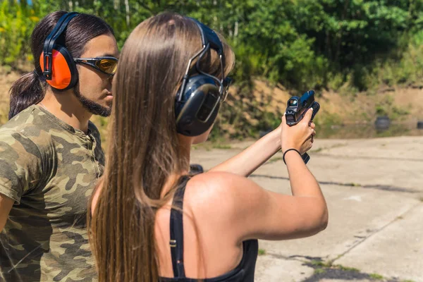 Rear view of white woman and man wearing safety goggles and headphones learning how to operate handgun. Firearms training at firing range. Horizontal shot. High quality photo