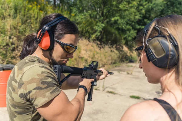 White man and woman in protective goggles and headphones at outdoor shooting range training with submachine gun. Firearms training, Outdoor horizontal shot. High quality photo