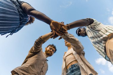 Multicultural group of young people standing in circle and holding their hands on top of each other. Unity, teamwork and support concept. High quality photo