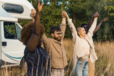 Group of happy young best friends raising and holding each others hands after reaching the destination of their camping van road trip. High quality photo