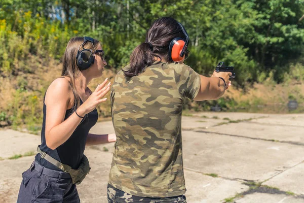 Two Europeans at a shooting range. Private shooting lessons. Female instructor and a man in moro t-shirt. Aiming at target. Outdoor shot. High quality photo