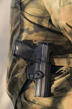 Vertical close-up shot of handgun in holster around soldiers waist. Camouflage army uniform. . High quality photo