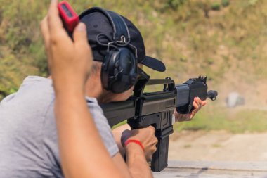 Rear view of man wearing safety headphones practicing firing shotgun on shooting range. Horizontal outdoor shot . High quality photo