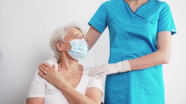 Glad calm caucasian pensioner laden white t-shirt, glasses and protective mask touching hands in gloves of an unrecognizable healthcare professional in turquoise uniform. High quality 4k footage
